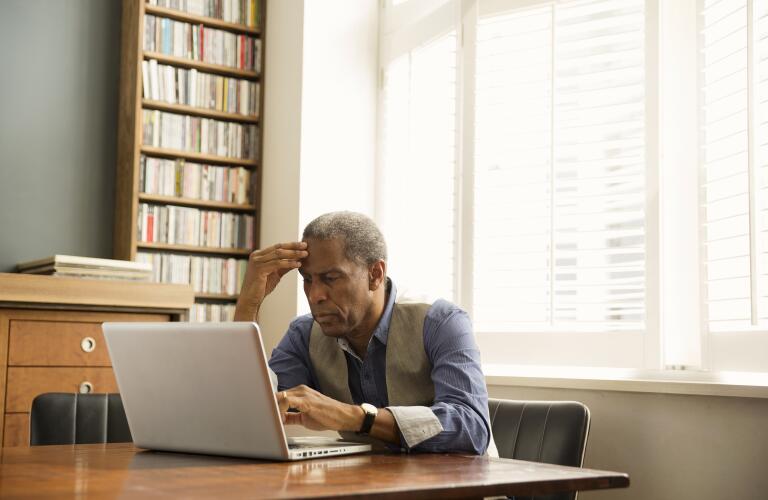 senior African American man sitting in office study looking at laptop