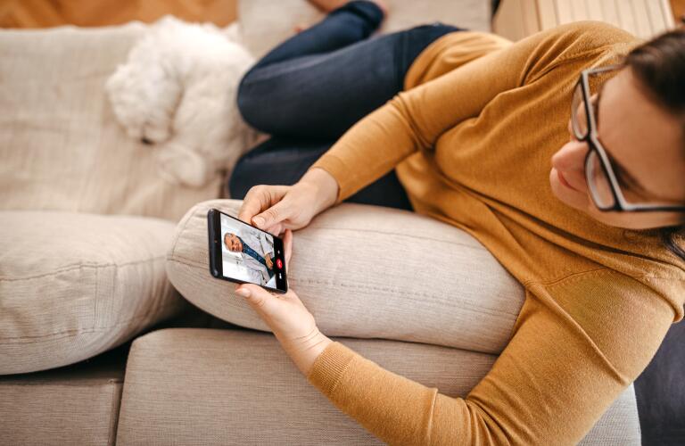 woman sitting on couch looking at smartphone during telehealth appointment