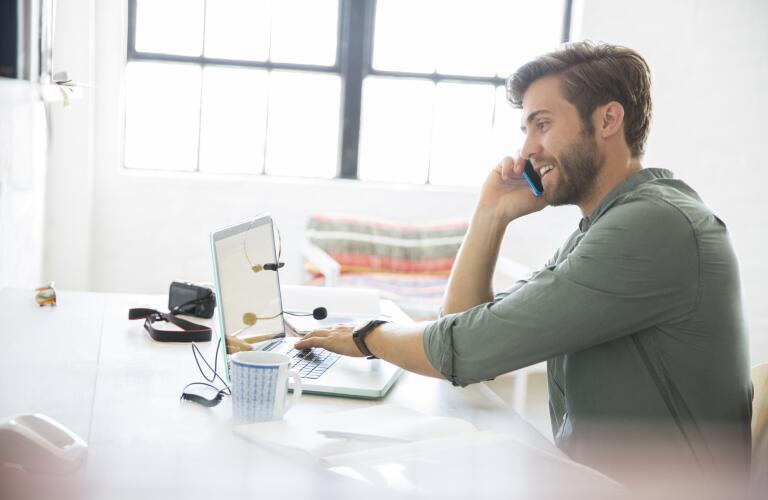 Portrait of young man sitting at desk with mobile phone and laptop