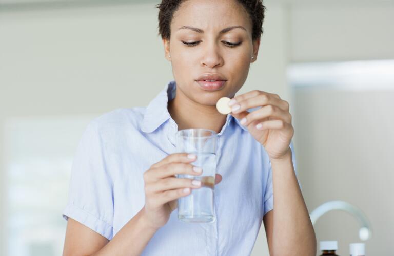 Young African American woman with indigestion using antacid tabletin glass of water